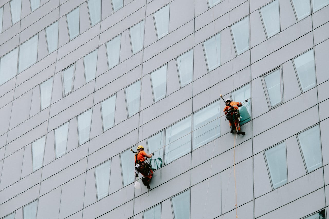 services-03 High-rise window washers in safety gear cleaning a skyscraper facade.