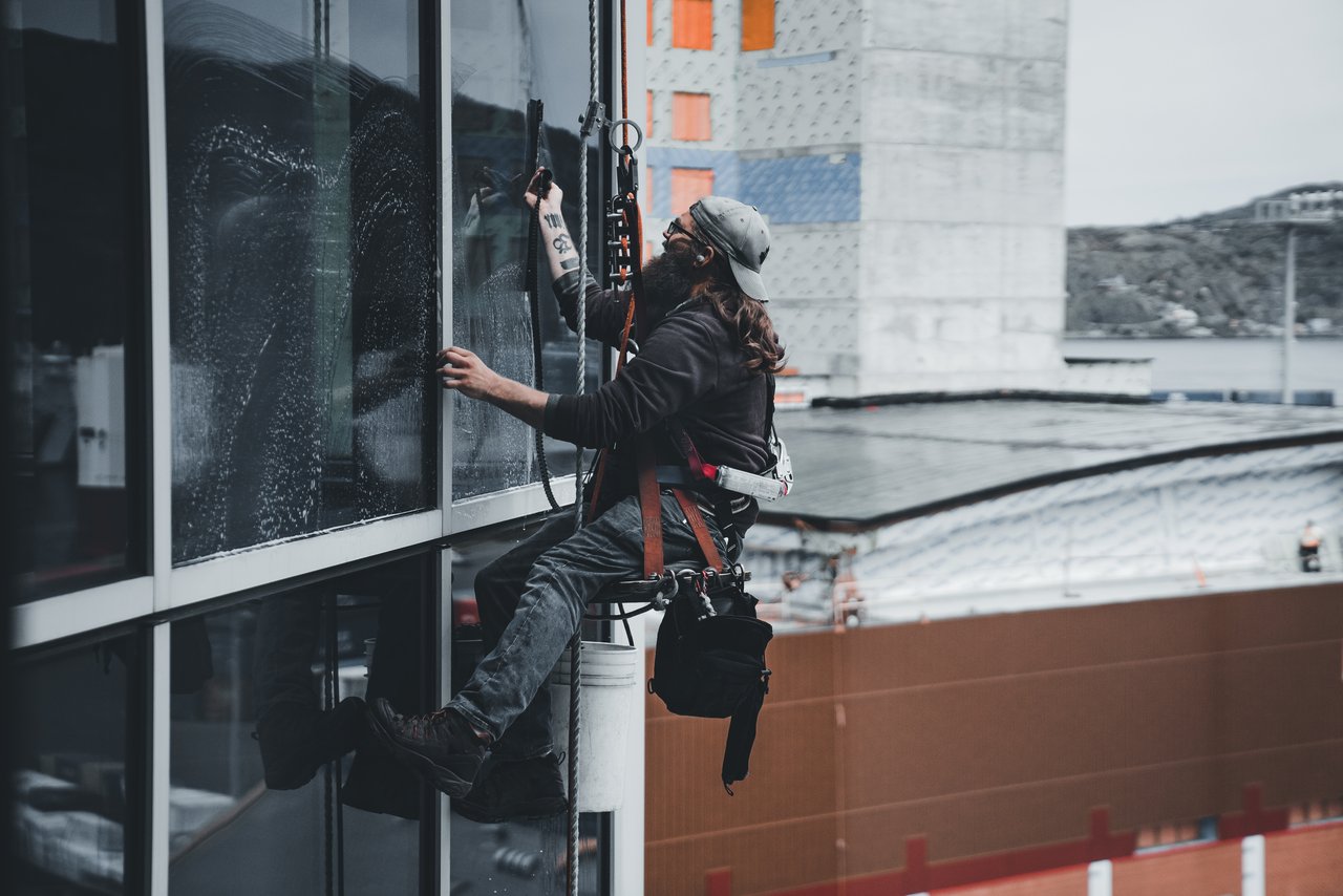 hero-img A man cleaning skyscraper windows with a harness, showcasing urban high-rise work.