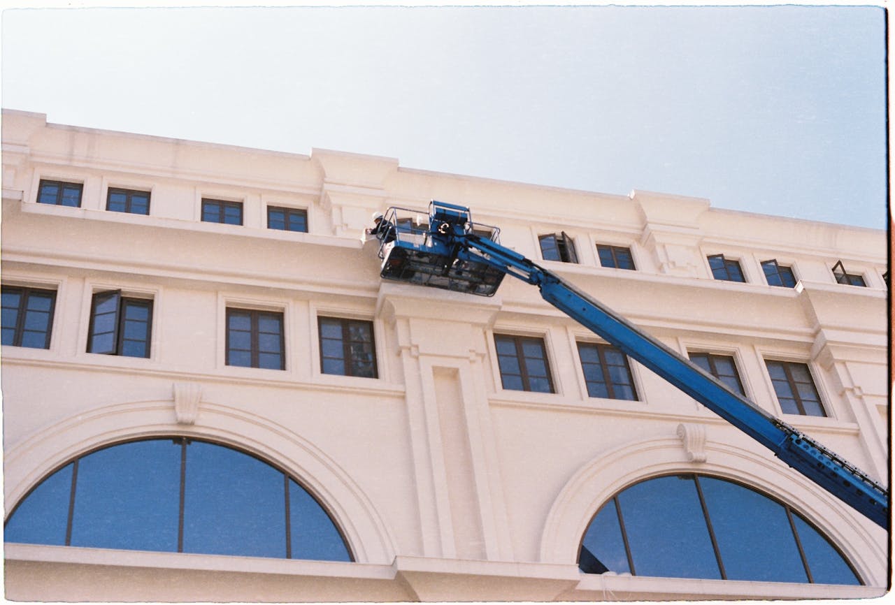 about-01 A worker cleans windows on a building using a blue crane on a clear day.